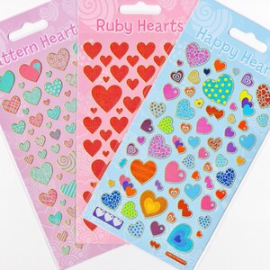 May include: Three sheets of heart-shaped stickers with gold outlines. The sheet on the left has a pink background with turquoise and pink patterned hearts. The middle sheet has a pink background with red glitter hearts. The sheet on the right has a blue background with colourful patterned hearts.
