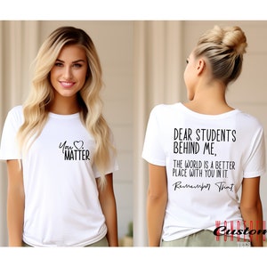 May include: White t-shirt with the text "You Matter" and a heart on the front. The back of the shirt has the text "Dear Students Behind Me, The World Is A Better Place With You In It. Remember That."