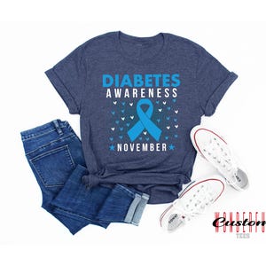 K&ouml;nnte beinhalten: Ein blaues T-Shirt mit dem Text "Diabetes Awareness November" und einem blauen Band. Das Shirt hat eine melierte blaue Farbe und ist aus einem weichen, bequemen Material gefertigt.