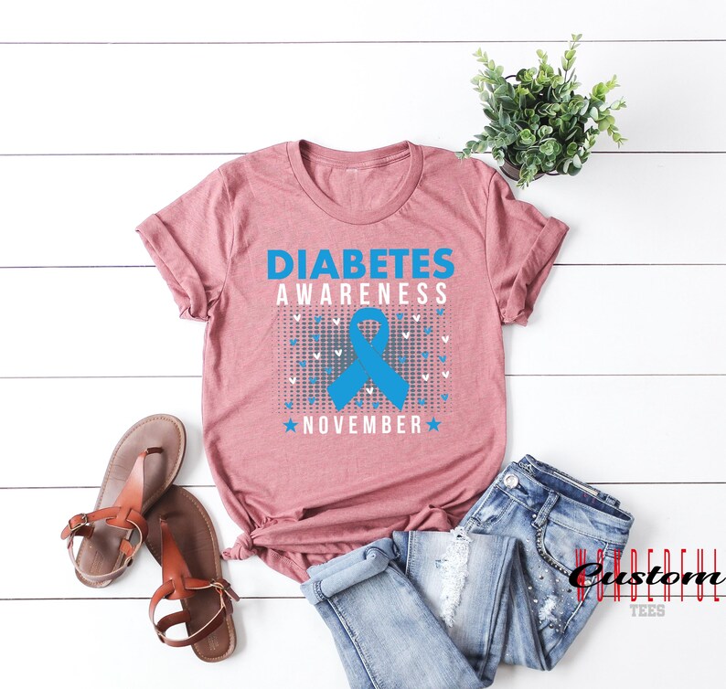 K&ouml;nnte beinhalten: Ein mauvefarbenes T-Shirt mit dem Text "Diabetes Awareness November" und einem blauen Band.
