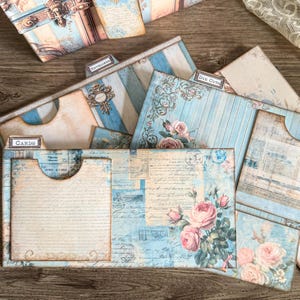 Printable French Country ephemera accordion storage suitcase kit in dusty blue, cream, and blush tones. Includes vintage-inspired suitcase panels, six coordinating folder inserts with toile, damask, and floral designs, matching backing paper, six small pockets, six elegant tags, and three luggage tags. Perfect for organizing and storing journaling supplies, scrapbooking materials, tickets, and keepsakes in a romantic French country style. Digital download for crafting.