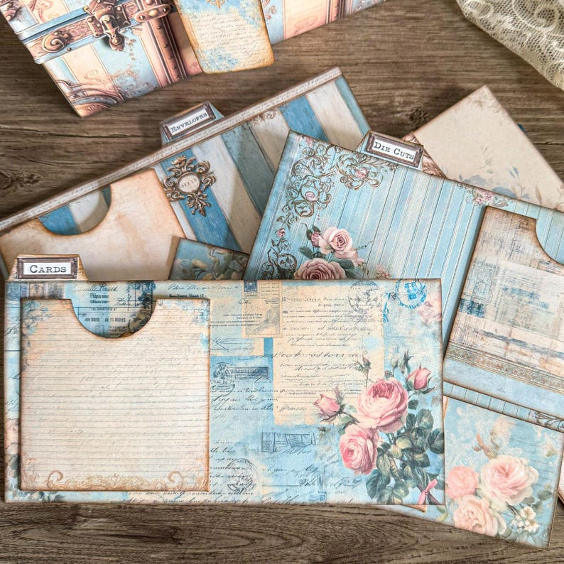 Printable French Country ephemera accordion storage suitcase kit in dusty blue, cream, and blush tones. Includes vintage-inspired suitcase panels, six coordinating folder inserts with toile, damask, and floral designs, matching backing paper, six small pockets, six elegant tags, and three luggage tags. Perfect for organizing and storing journaling supplies, scrapbooking materials, tickets, and keepsakes in a romantic French country style. Digital download for crafting.