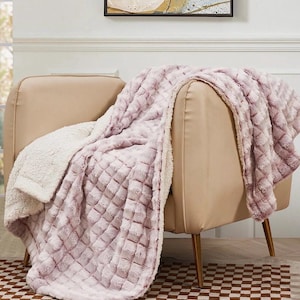 May include: A plush, lavender throw blanket with a diamond pattern is draped over a beige armchair. The blanket has a soft, textured surface and a cream-colored, fuzzy underside. The chair has gold-colored legs and sits on a checkered rug.