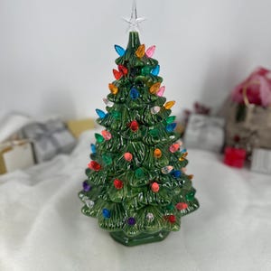 May include: A ceramic Christmas tree with a glossy green finish. The tree is decorated with colourful, plastic lights and topped with a clear star. A classic festive decoration.