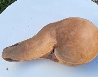 May include: A handcrafted wooden bowl with a natural, light brown finish. The bowl has a unique, organic shape with a smooth, polished surface. The wood grain is visible, adding to its rustic charm. The bowl is approximately 18 inches long.