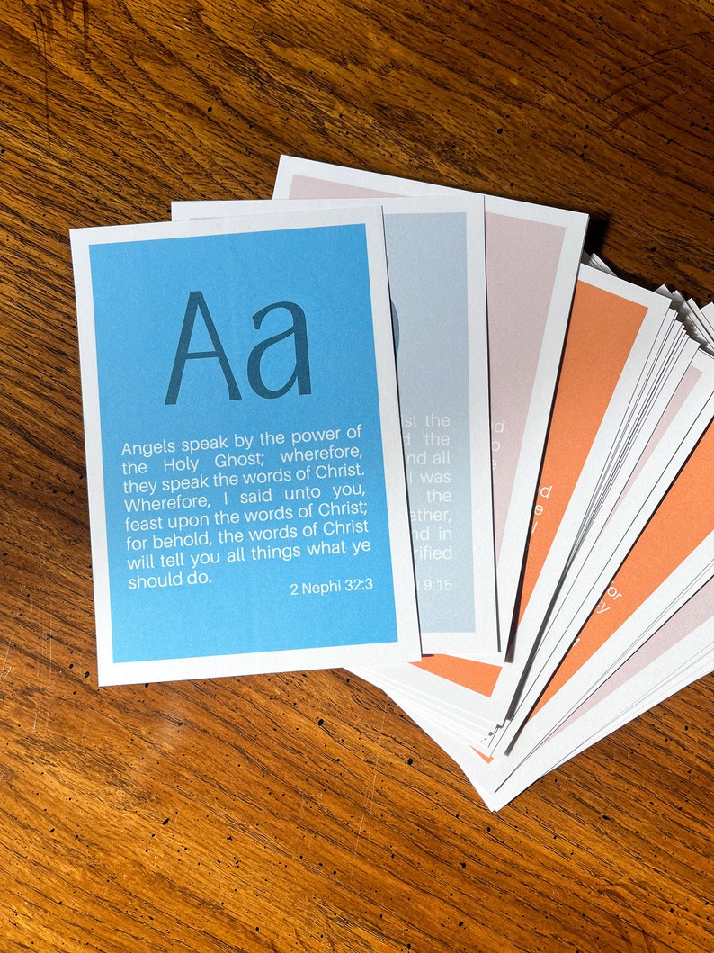 May include: A blue card with the letter "Aa" in large, bold, white font. The card has a quote from the Book of Mormon, 2 Nephi 32:3, about the power of angels and the words of Christ.