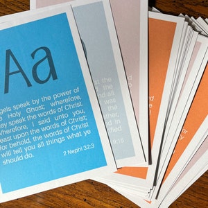 May include: A stack of cards with different coloured backgrounds. The top card is blue and features the letter "Aa" in a large font. The text "gels speak by the power of the Holy Ghost; wherefore, they speak the words of Christ. Wherefore, I said unto you, feast upon the words of Christ; for behold, the words of Christ will tell you all things what ye should do. 2 Nephi 32:3" is printed on the card.