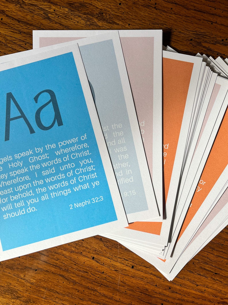 May include: A stack of cards with different coloured backgrounds. The top card is blue and features the letter "Aa" in a large font. The text "gels speak by the power of the Holy Ghost; wherefore, they speak the words of Christ. Wherefore, I said unto you, feast upon the words of Christ; for behold, the words of Christ will tell you all things what ye should do. 2 Nephi 32:3" is printed on the card.