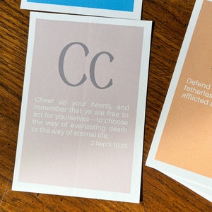 May include: A light pink card with the letters "CC" in grey. The card has the text "Cheer up your hearts, and remember that ye are free to act for yourselves to choose the way of everlasting death or the way of eternal life. 2 Nephi 10:23"
