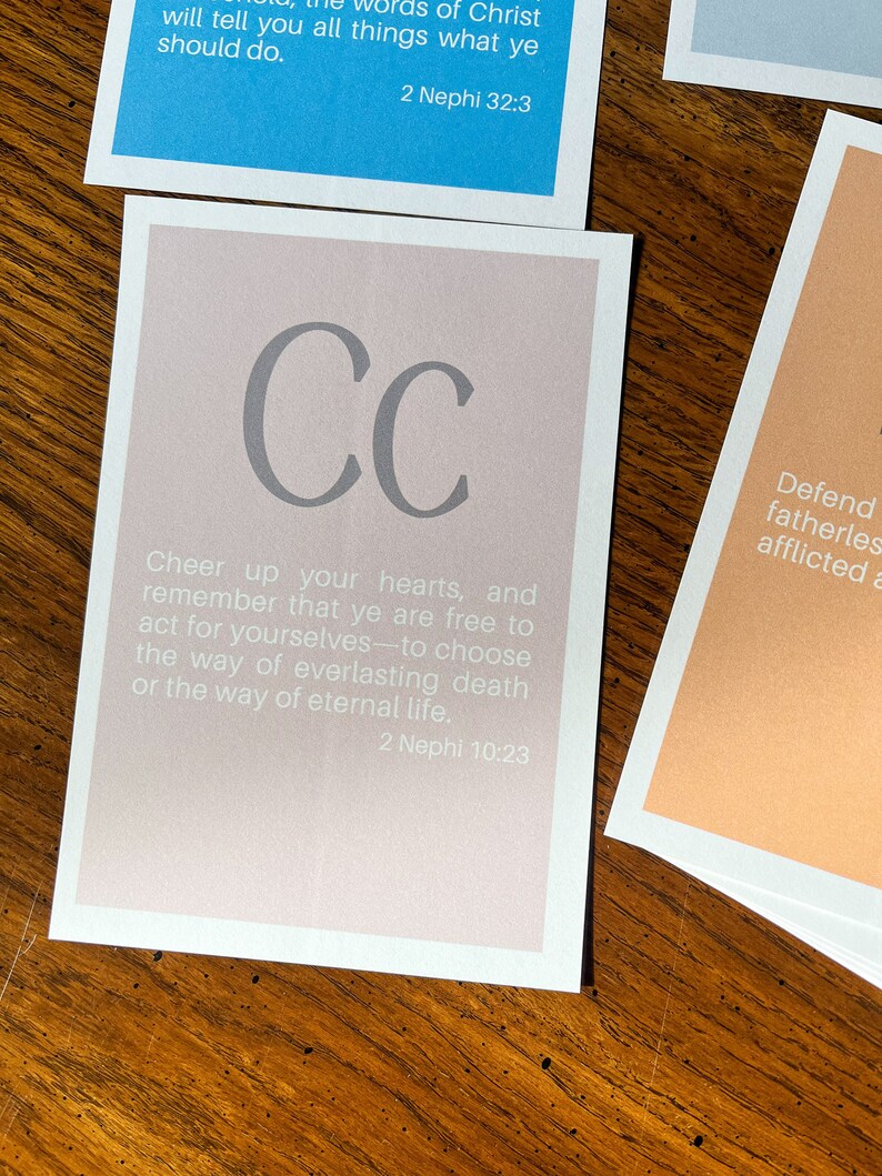May include: A light pink card with the letters "CC" in grey. The card has the text "Cheer up your hearts, and remember that ye are free to act for yourselves to choose the way of everlasting death or the way of eternal life. 2 Nephi 10:23"