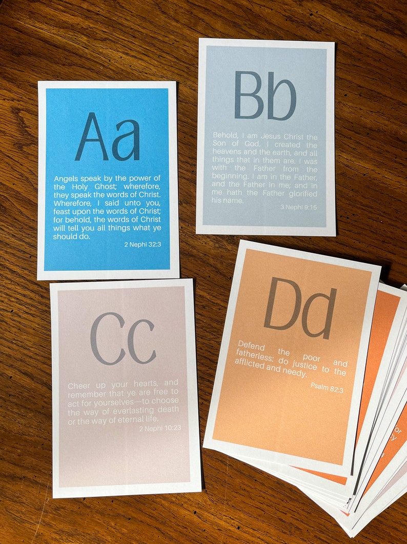 May include: A set of alphabet flashcards with a scripture quote on each card. The cards are in different colours, including blue, light blue, pink, and orange. The letters are in a large, bold font. The quotes are from the Book of Mormon and the Bible.