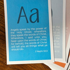 May include: A blue card with the letter "Aa" in a large font at the top. The card has a quote from the Book of Mormon, 2 Nephi 32:3, which reads: "Angels speak by the power of the Holy Ghost; wherefore, they speak the words of Christ. Wherefore, I said unto you, feast upon the words of Christ; for behold, the words of Christ will tell you all things what ye should do."