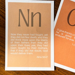 May include: A light orange card with the letter "N" in a brown font. The card has a quote from the Book of Mormon, Alma 56:47, which reads: "Now they never had fought, yet they did not fear death; and they did think more upon the liberty of their fathers than they did upon their lives; yea, they had been taught by their mothers, that if they did not doubt, God would deliver them."