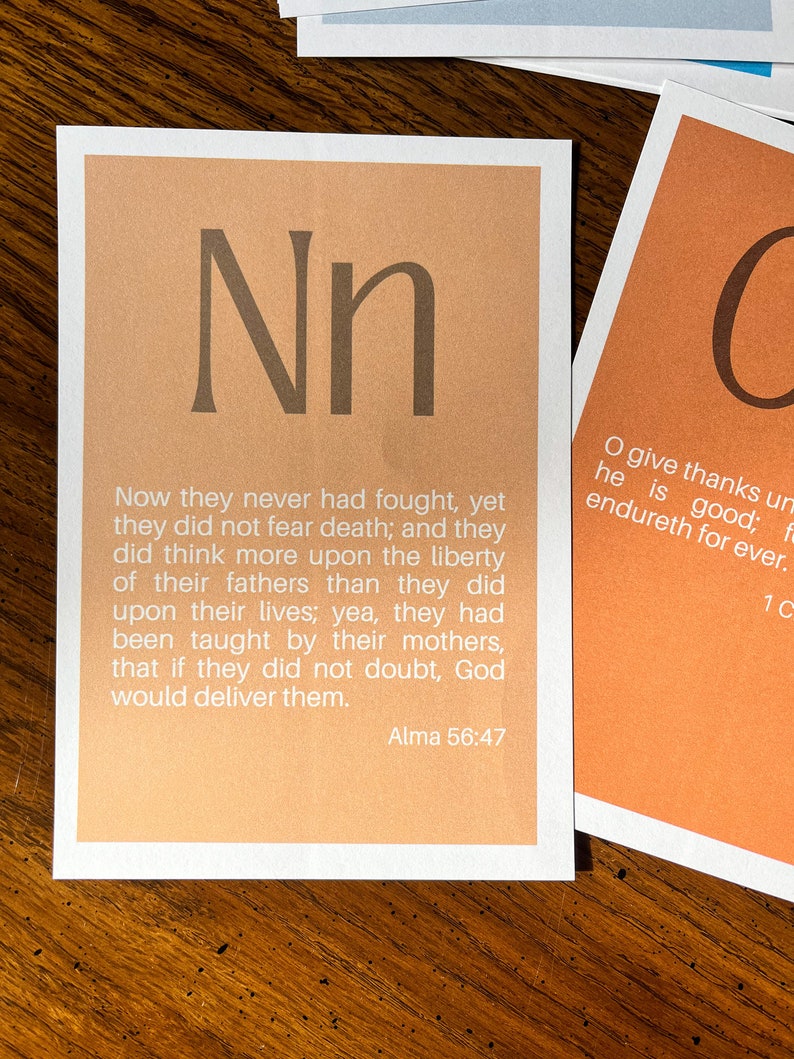 May include: A light orange card with the letter "N" in a brown font. The card has a quote from the Book of Mormon, Alma 56:47, which reads: "Now they never had fought, yet they did not fear death; and they did think more upon the liberty of their fathers than they did upon their lives; yea, they had been taught by their mothers, that if they did not doubt, God would deliver them."