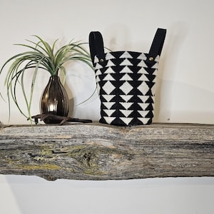 May include: A black and white geometric patterned fabric storage basket with black leather handles. The basket is sitting on a rustic wooden shelf.