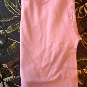 Op de afbeelding: Een effen lichtroze sweatshirt, netjes opgevouwen. De stof lijkt een zacht materiaal te zijn. De sweatshirt is effen van kleur, zonder zichtbare afbeeldingen of patronen. Het kledingstuk is waarschijnlijk voor vrijetijdsgebruik.
