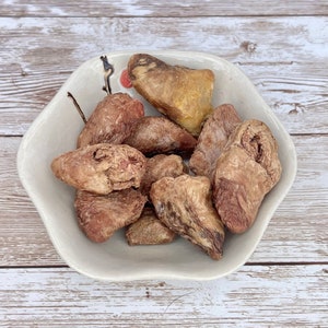 May include: A white ceramic bowl filled with dried meat treats for dogs. The treats are brown and have a chewy texture.