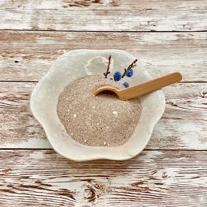 May include: A white ceramic bowl with a blue floral design, filled with a light brown powder and a wooden spoon.