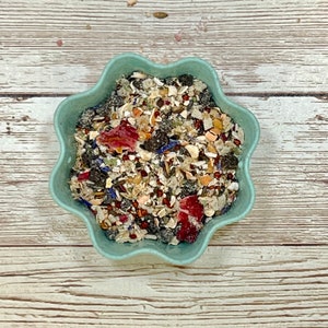 May include: A teal blue bowl filled with a mixture of dried fruits, seeds, and herbs. The bowl has a scalloped edge.