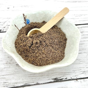 May include: A white ceramic bowl filled with a brown powder, a small wooden spoon is resting in the bowl.