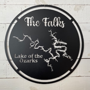 May include: Black metal sign with the text "The Falks" and "Lake of the Ozarks" in a white outline. The sign features a cutout of the Lake of the Ozarks.