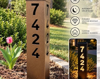 May include: A tall, rectangular, bronze-coloured metal address post featuring the cutout numbers 7424 on the front and side. The top includes a solar panel, and the post illuminates from within, displaying the numbers as glowing light at night.