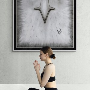 K&ouml;nnte beinhalten: Eine Frau sitzt in einer Yoga-Pose auf einer schwarzen Yogamatte mit geometrischem Muster. Sie tr&auml;gt schwarze Leggings und einen schwarzen Sport-BH. Hinter ihr befindet sich eine gerahmte Schwarzwei&szlig;zeichnung eines Adlergesichts. Die Zeichnung ist mit "El Shaddai" signiert und mit "01.03.20" datiert.