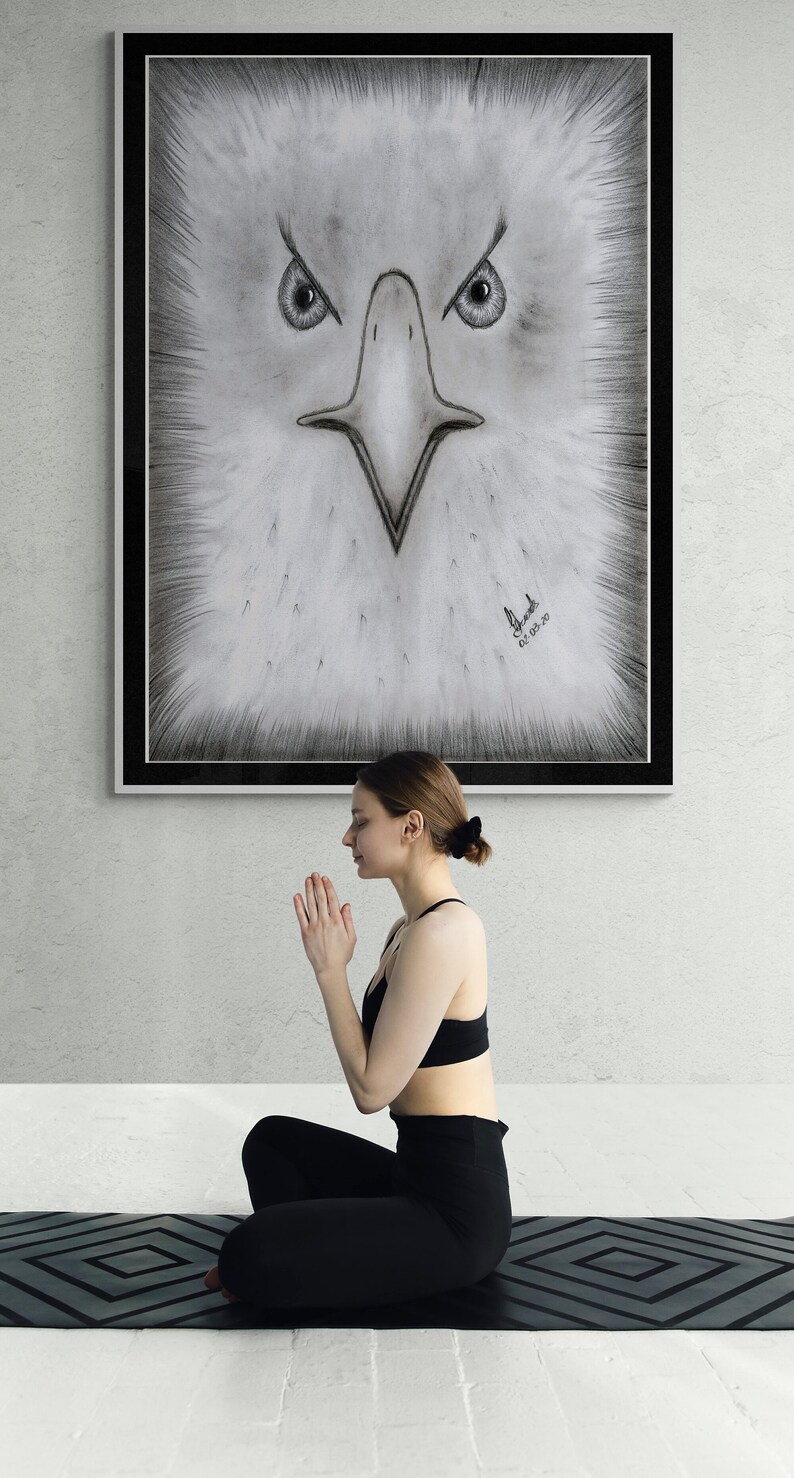 K&ouml;nnte beinhalten: Eine Frau sitzt in einer Yoga-Pose auf einer schwarzen Yogamatte mit geometrischem Muster. Sie tr&auml;gt schwarze Leggings und einen schwarzen Sport-BH. Hinter ihr befindet sich eine gerahmte Schwarzwei&szlig;zeichnung eines Adlergesichts. Die Zeichnung ist mit "El Shaddai" signiert und mit "01.03.20" datiert.