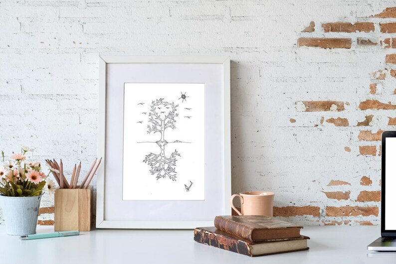 May include: A black and white line drawing of a tree with roots and birds flying above. The drawing is framed in a white frame and is sitting on a white surface with a cup, pencils, and books.