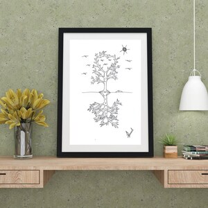 May include: Black and white line art print of a tree with roots and birds flying above. The print is framed in a black frame and hanging on a green wall above a wooden desk.