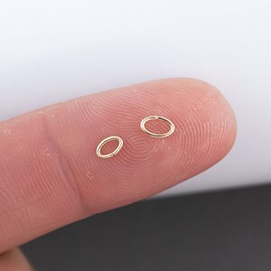 May include: Two gold jump rings, one larger than the other, are held between two fingers.