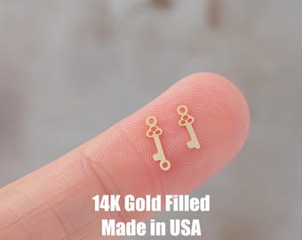 Op de afbeelding: Twee goudgevulde sleutelbedels, elk met een kleine lus aan de bovenkant. De bedels bevinden zich op een vinger, en de tekst "14K Gold Filled Made in USA" bevindt zich eronder.