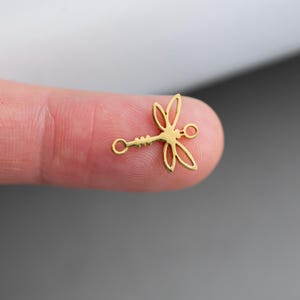 May include: Gold-toned metal dragonfly charm with two jump rings. The charm is in the shape of a dragonfly with delicate wings and a long, slender body.