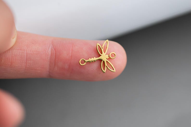 Op de afbeelding: Goudkleurige metalen libel charm met twee springringen. De charm is in de vorm van een libel met delicate vleugels en een lang, slank lichaam.