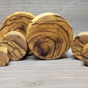 May include: A set of 12 wooden ear gauges in various sizes, featuring a natural wood grain pattern with dark brown streaks. The gauges are round and have a smooth, polished finish.