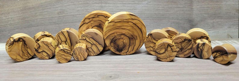May include: A set of 12 wooden ear gauges in various sizes, featuring a natural wood grain pattern with dark brown streaks. The gauges are round and have a smooth, polished finish.