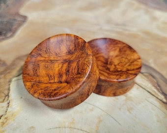 May include: Two wooden ear gauges, one brown and one reddish brown, with a swirling wood grain pattern.