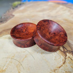 May include: Two wooden ear gauges with a reddish-brown colour and a swirling grain pattern.