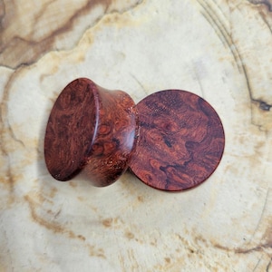 May include: Two wooden ear gauges, one round and one flared, with a reddish-brown wood grain pattern.