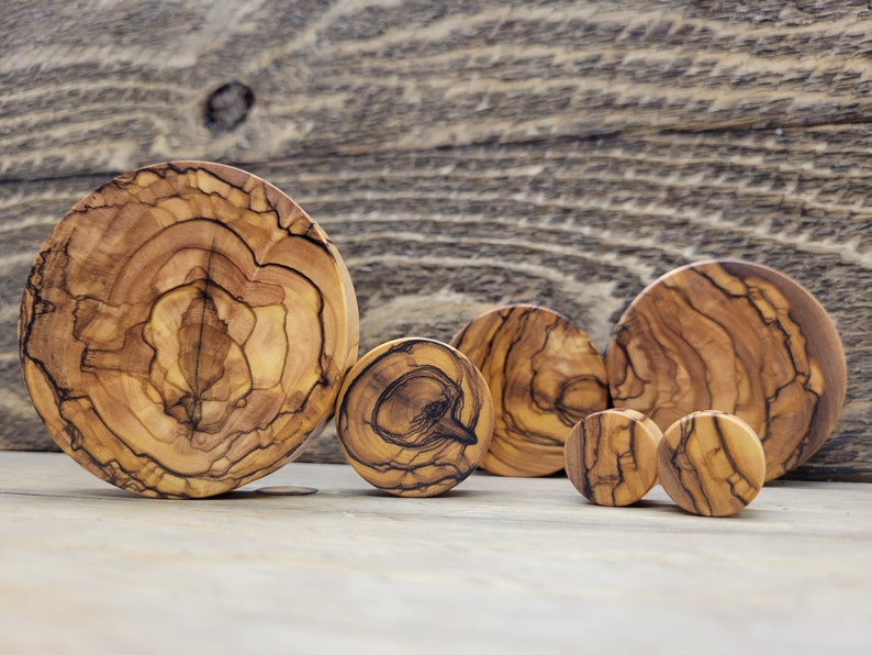 May include: A set of six olive wood ear gauges in various sizes. The gauges are round and have a natural wood grain pattern.