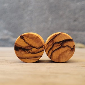 May include: Two round wooden ear gauges with a natural wood grain pattern. The gauges have a dark brown and light brown color.