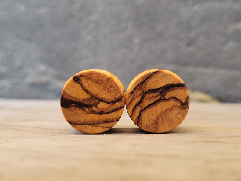 May include: Two round wooden ear gauges with a natural wood grain pattern. The gauges have a dark brown and light brown color.