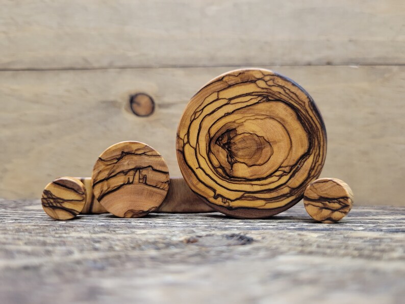 May include: Four wooden ear gauges of varying sizes, made from olive wood with a natural brown and black grain pattern.