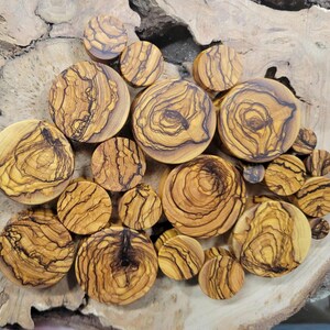 May include: A collection of olive wood ear gauges in various sizes and patterns. The gauges are a natural wood colour with dark brown streaks and swirls.