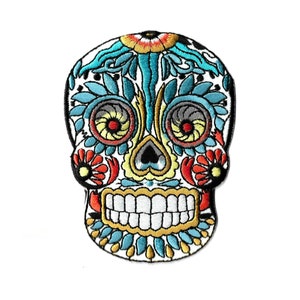May include: Embroidered skull patch with a Day of the Dead design. The patch features a white background with colorful floral and decorative elements in teal, red, yellow, and black. The skull has a detailed, smiling mouth.