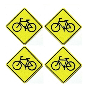 May include: Four yellow diamond-shaped patches with a black bicycle symbol. The bicycle symbol is centered within the yellow diamond. The patches are arranged in a two-by-two grid against a white background.