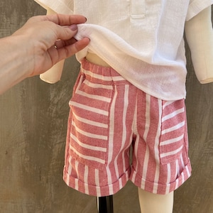 May include: Red and white striped shorts with cuffed hems. The shorts have two pockets on the front.