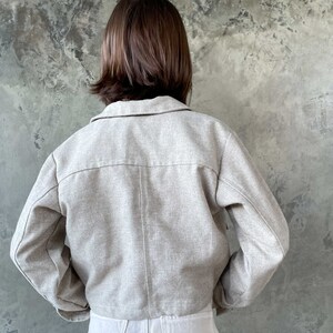 May include: A light beige cropped jacket with long sleeves and a button-up front.