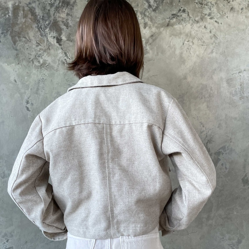 May include: A light beige cropped jacket with long sleeves and a button-up front.