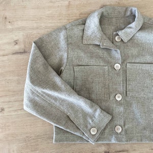 May include: A gray cropped jacket with long sleeves and four buttons down the front. The jacket has two large pockets on the front.